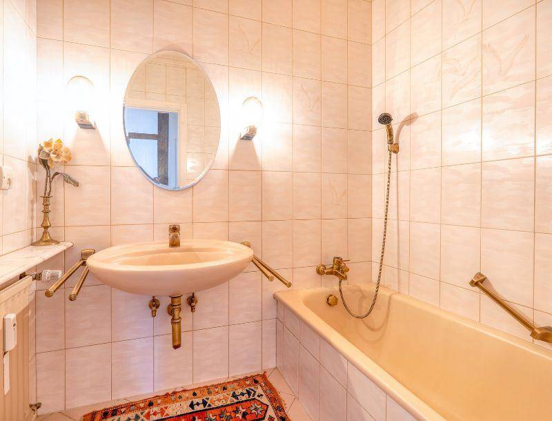 Helles Badezimmer mit beigefarbenen Fliesen, Badewanne und Waschtisch mit Spiegel.