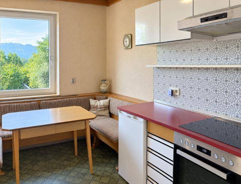 Gemütliche Küche mit Essecke, roter Arbeitsplatte, weißen Schränken und Fenster mit Grünblick.