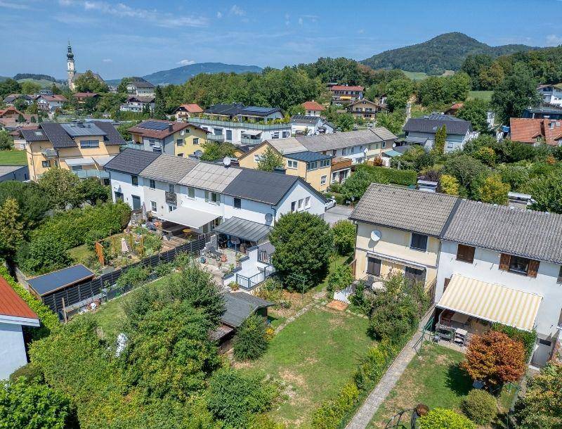 Luftaufnahme einer Wohnsiedlung mit Häusern, Gärten und einem Kirchturm im Hintergrund.