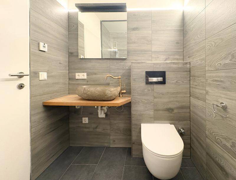 Modernes Badezimmer mit holzgemusterten Fliesen, einem einzigartigen Steinswaschbecken und Wand-WC.