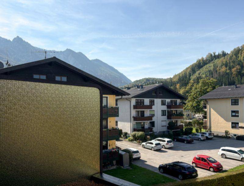 Blick auf umliegende Gebäude und einen Parkplatz mit majestätischen Bergen im Hintergrund unter blauem Himmel.