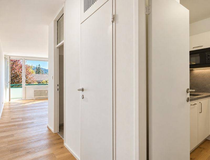Heller Flur mit Holzboden, der zu einem Wohnbereich und einer Küchenzeile führt.