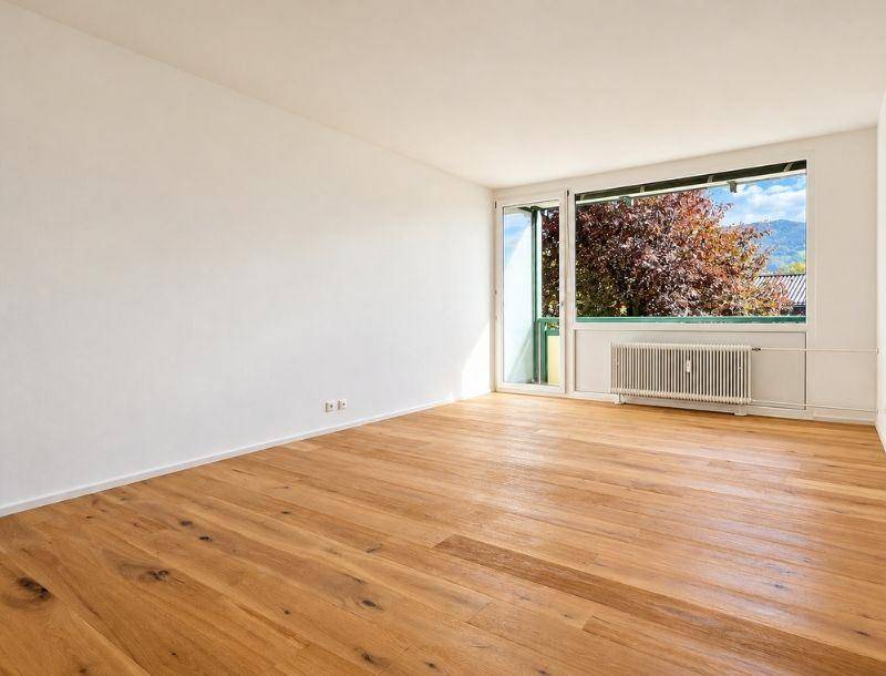 Heller Raum mit neuem Parkettboden und großem Fenster mit Zugang zum Balkon und Bergblick.