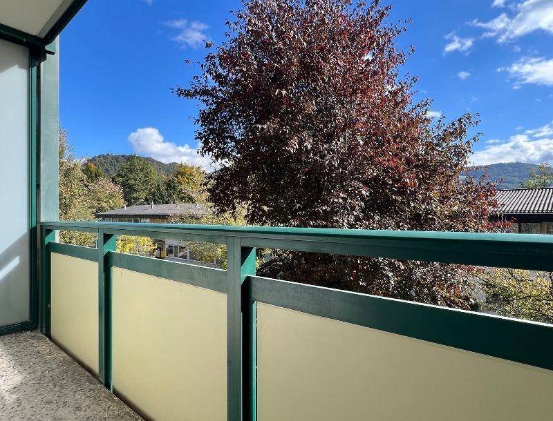 Balkon mit grüner Brüstung und Blick auf Bäume sowie die umliegende Berglandschaft.
