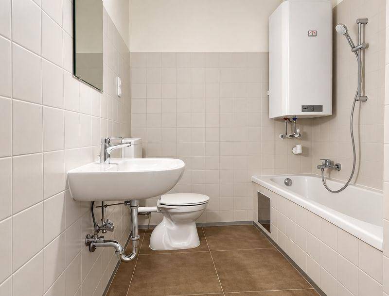 Funktionales Badezimmer mit Badewanne, Waschbecken, Toilette und Wandfliesen in neutralen Farben.