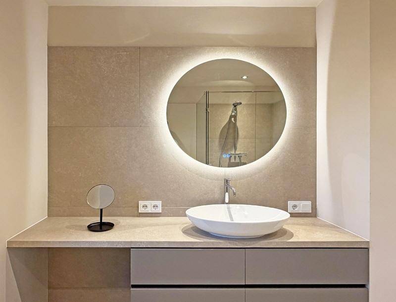 Modernes Badezimmer mit beleuchtetem Spiegel, Aufsatzwaschbecken und großformatigen Fliesen, elegant gestaltet.