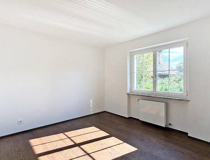 Helles Zimmer mit dunklem Holzboden und einem Fenster, das viel Tageslicht hereinlässt, ideal als Schlafzimmer.