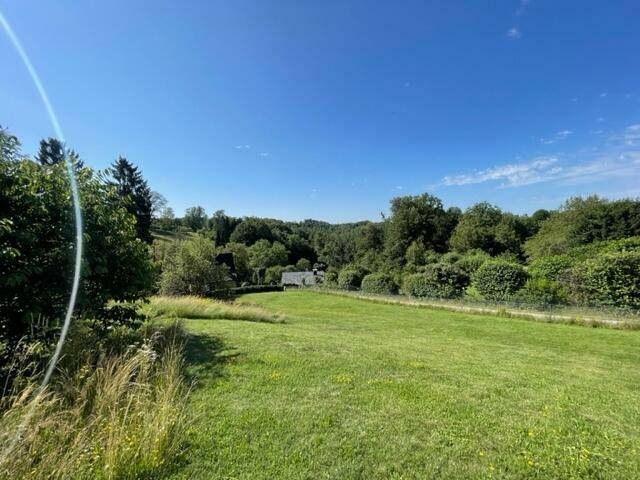 Weitläufige grüne Landschaft mit sanften Hügeln und vereinzelten Häusern unter blauem Himmel.