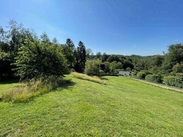 Weitläufige grüne Landschaft mit sanften Hügeln und vereinzelten Häusern unter blauem Himmel.