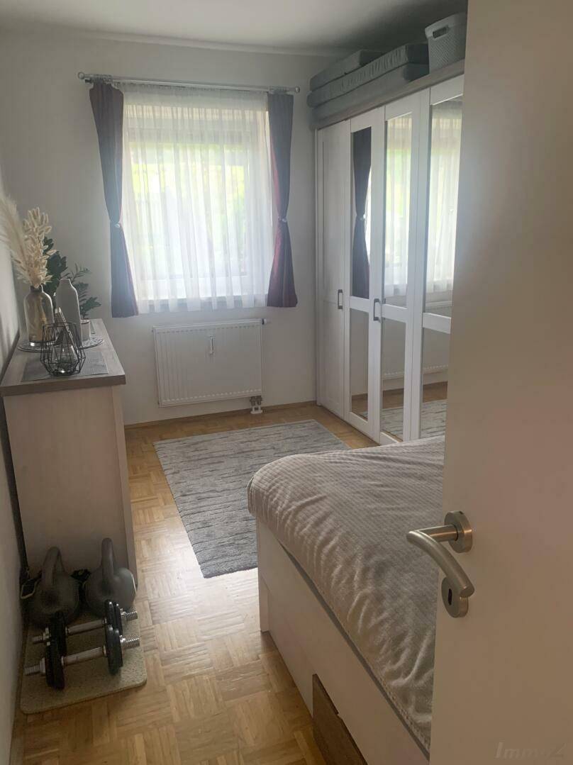 Schlafzimmer mit Holzboden, großem Fenster, Spiegelschrank und Hanteln für Fitness.