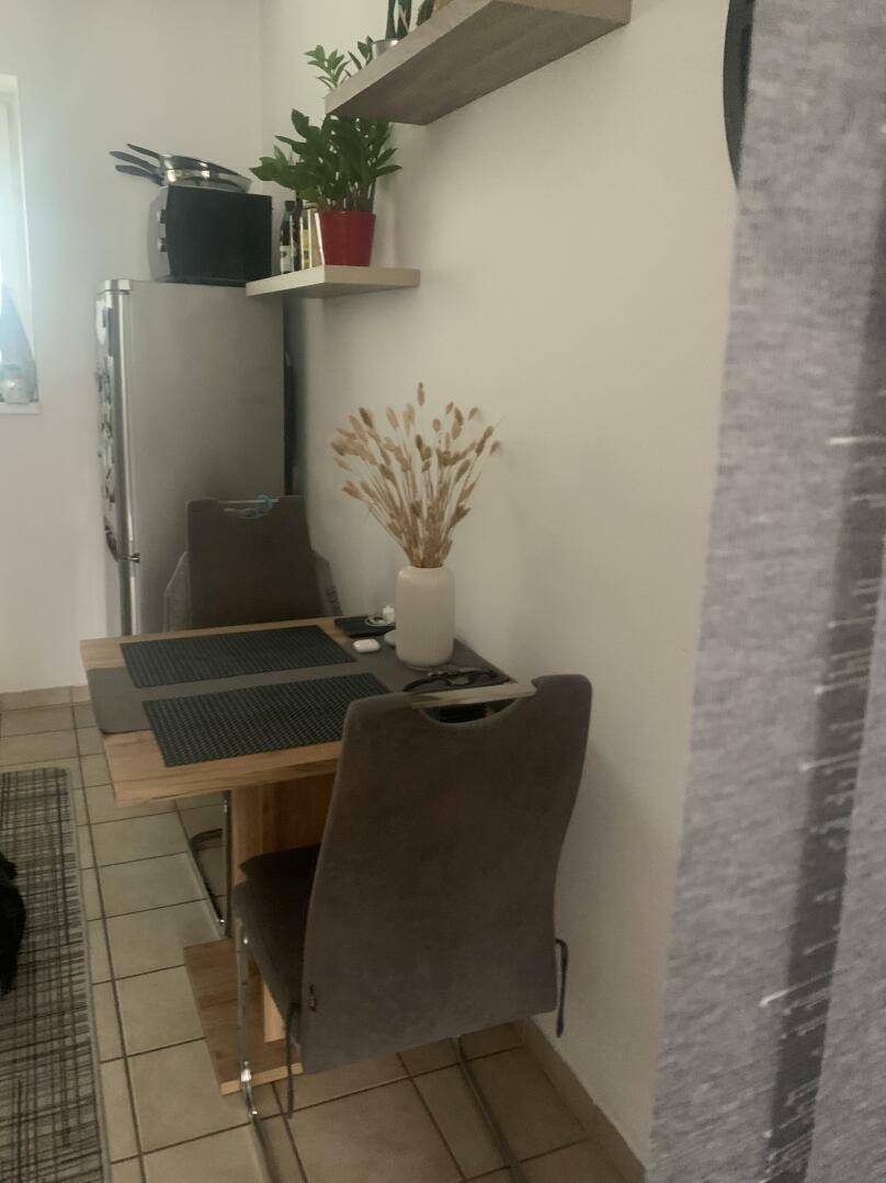 Kleiner Essbereich mit Holztisch, zwei Stühlen und einem Kühlschrank, ideal für Mahlzeiten.
