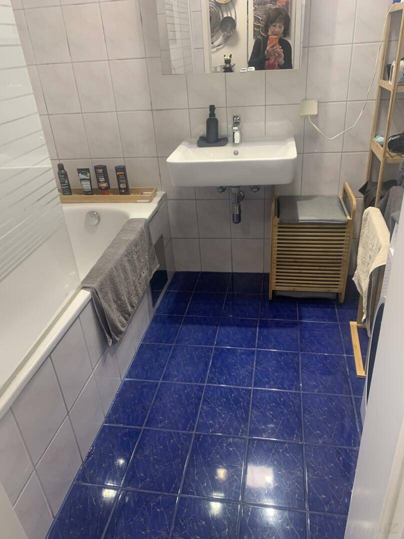 Badezimmer mit blauen Bodenfliesen, Badewanne, Waschbecken und Spiegelschrank, hell beleuchtet.