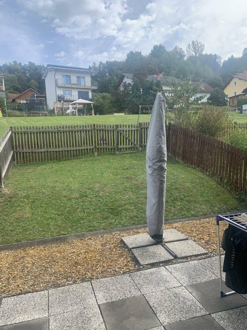 Großer grüner Garten mit Rasenfläche, Holzzaun und Blick auf weitere Häuser in der Ferne.