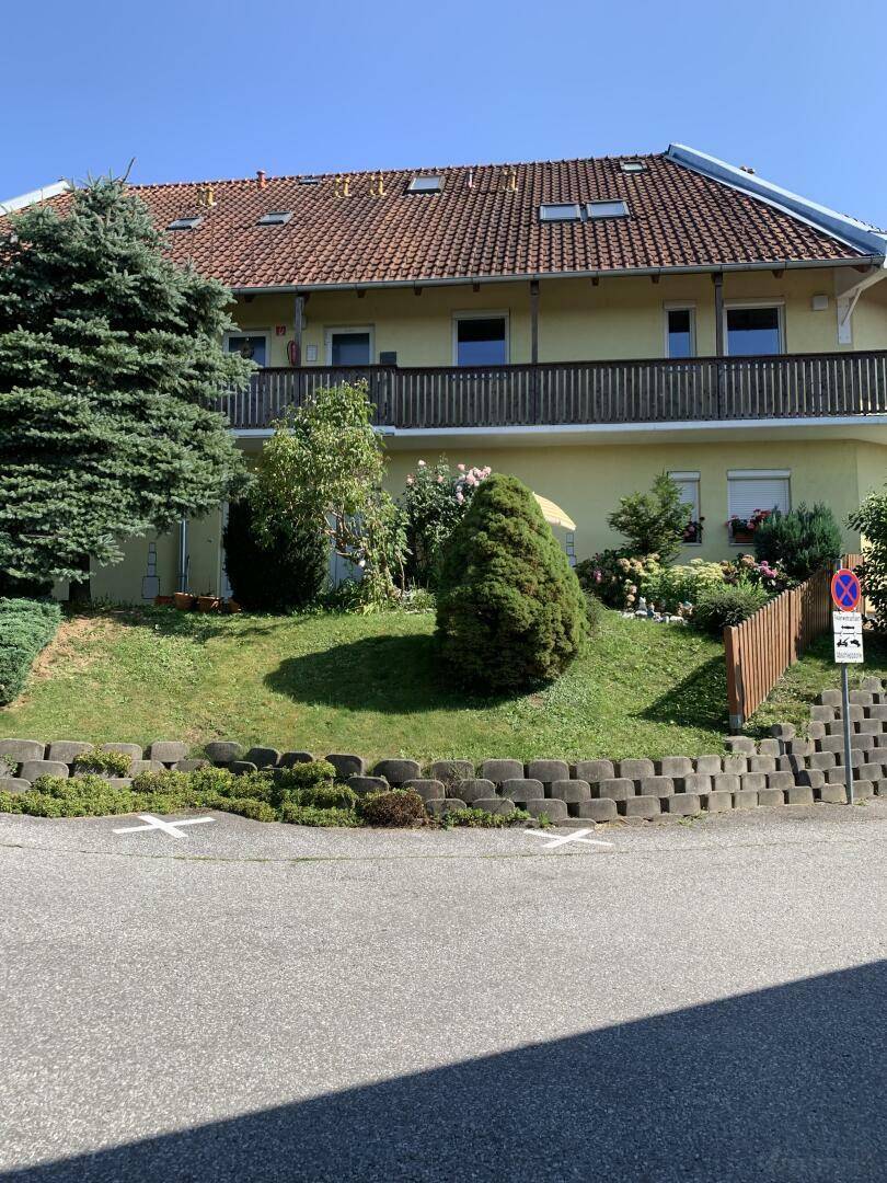 Ansicht eines gelben Mehrfamilienhauses mit Balkonen und gepflegtem Vorgarten an einem sonnigen Tag.