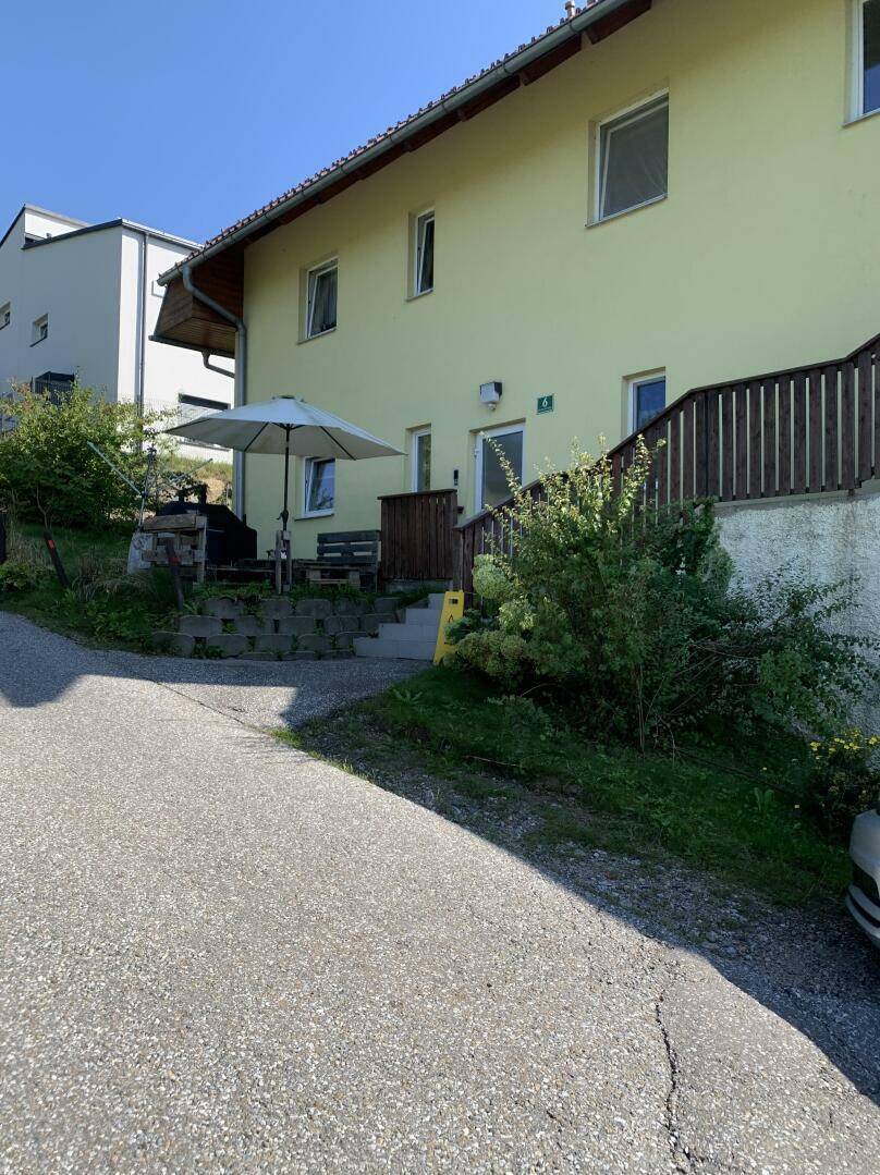 Seitlicher Eingangsbereich des Hauses mit einer kleinen Terrasse, Sonnenschirm und Sitzgelegenheit.