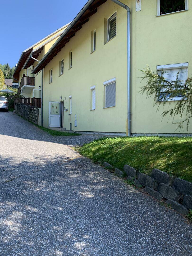 Seitenansicht des gelben Gebäudes mit Zufahrt und gepflegter Grünfläche an einem sonnigen Tag.