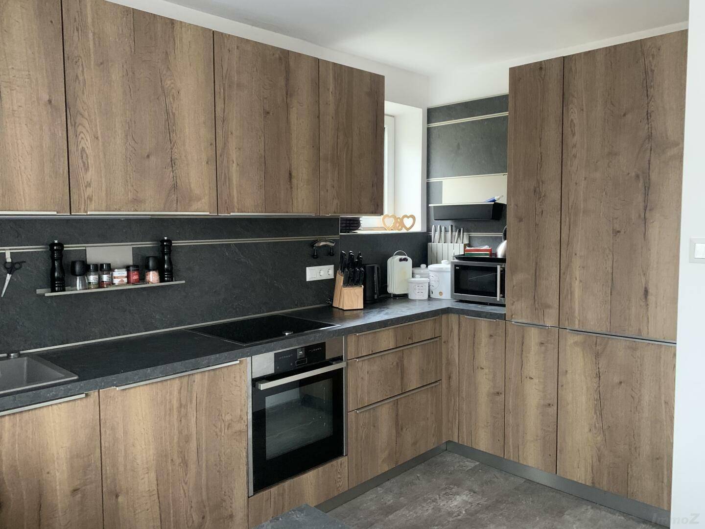 Moderne Küche mit Holzfronten, dunkler Arbeitsplatte und integrierten Geräten.