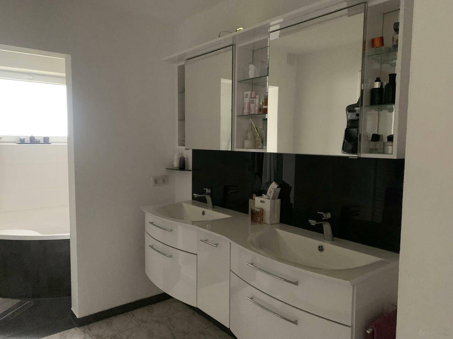 Modernes Badezimmer mit Doppelwaschbecken, Spiegelschrank und Badewanne im Hintergrund.