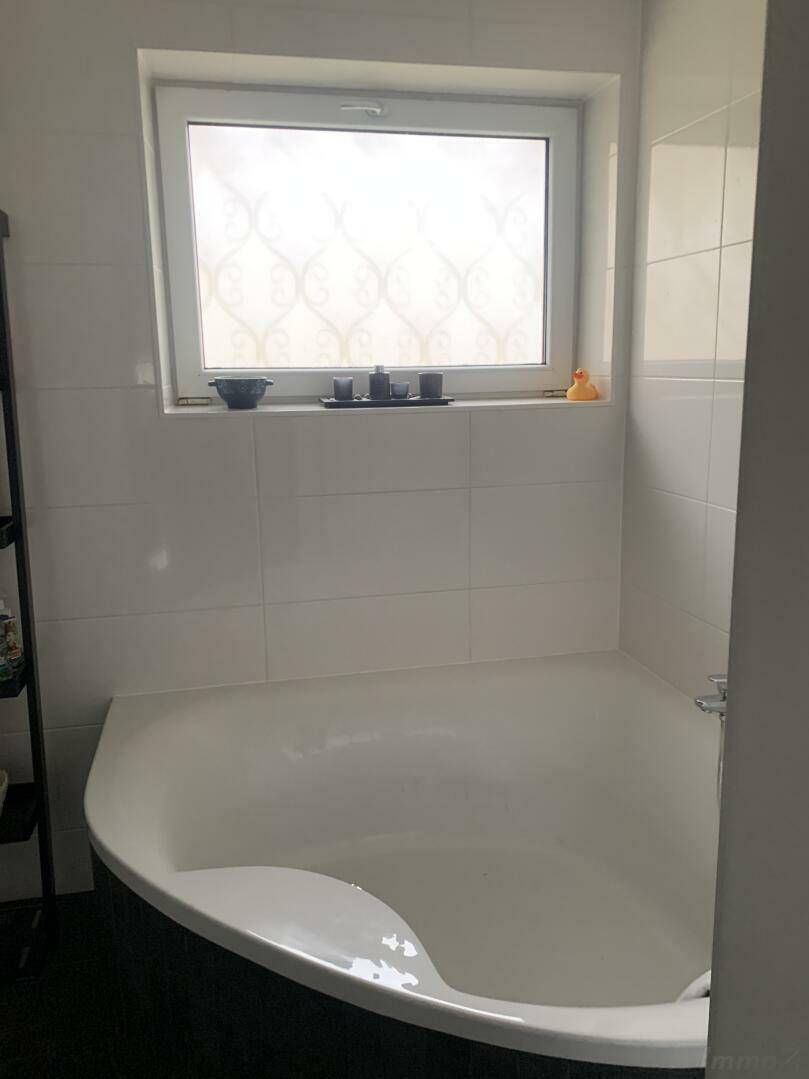 Eckbadewanne in einem hellen Badezimmer mit Fenster und weißen Fliesen.