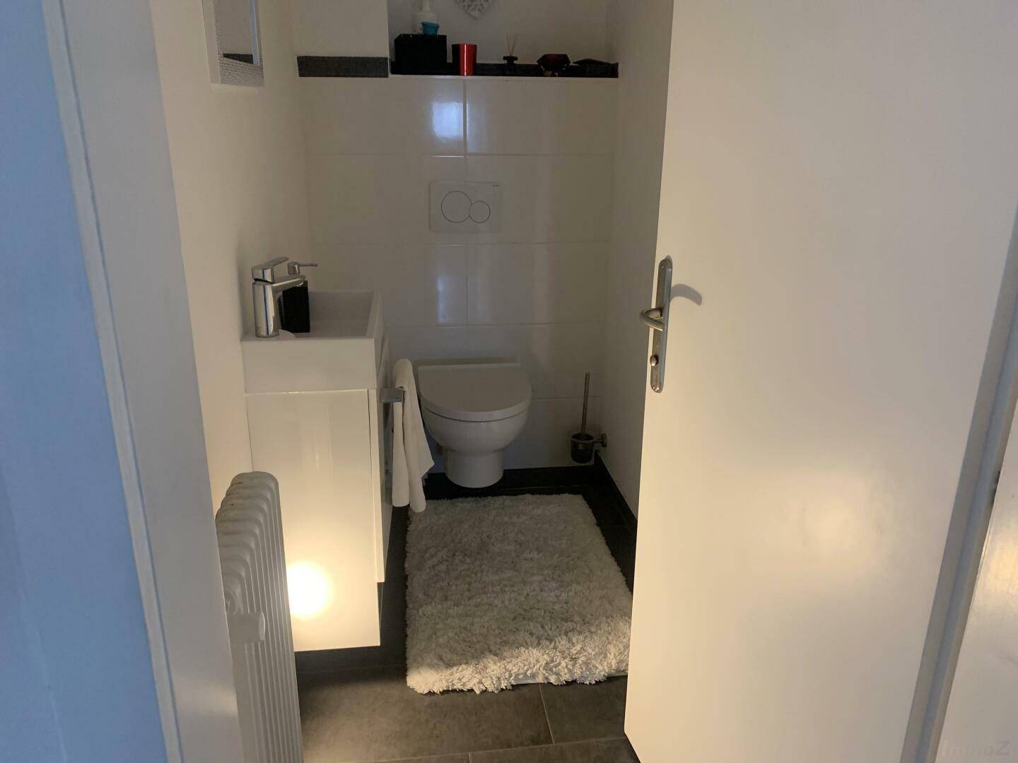 Kleines Gäste-WC mit modernem Waschbecken, Toilette und dunklem Fliesenboden.