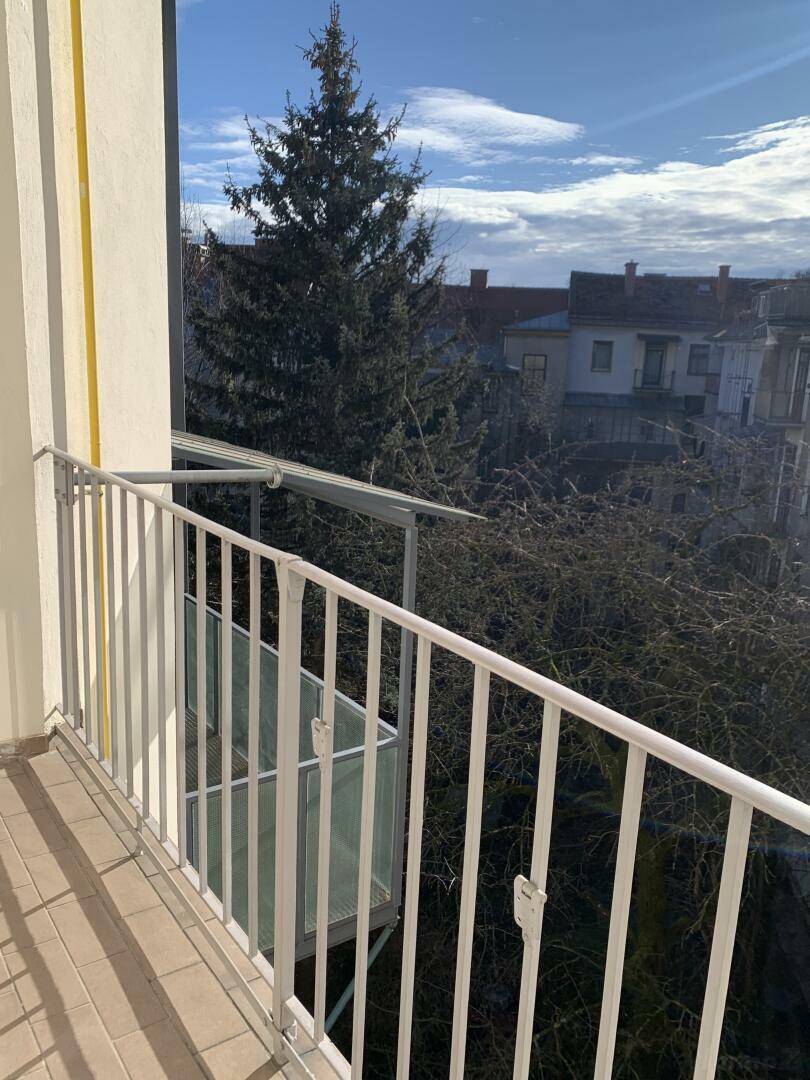 Kleiner Balkon mit Metallgeländer und Blick auf Bäume und umliegende Gebäude.