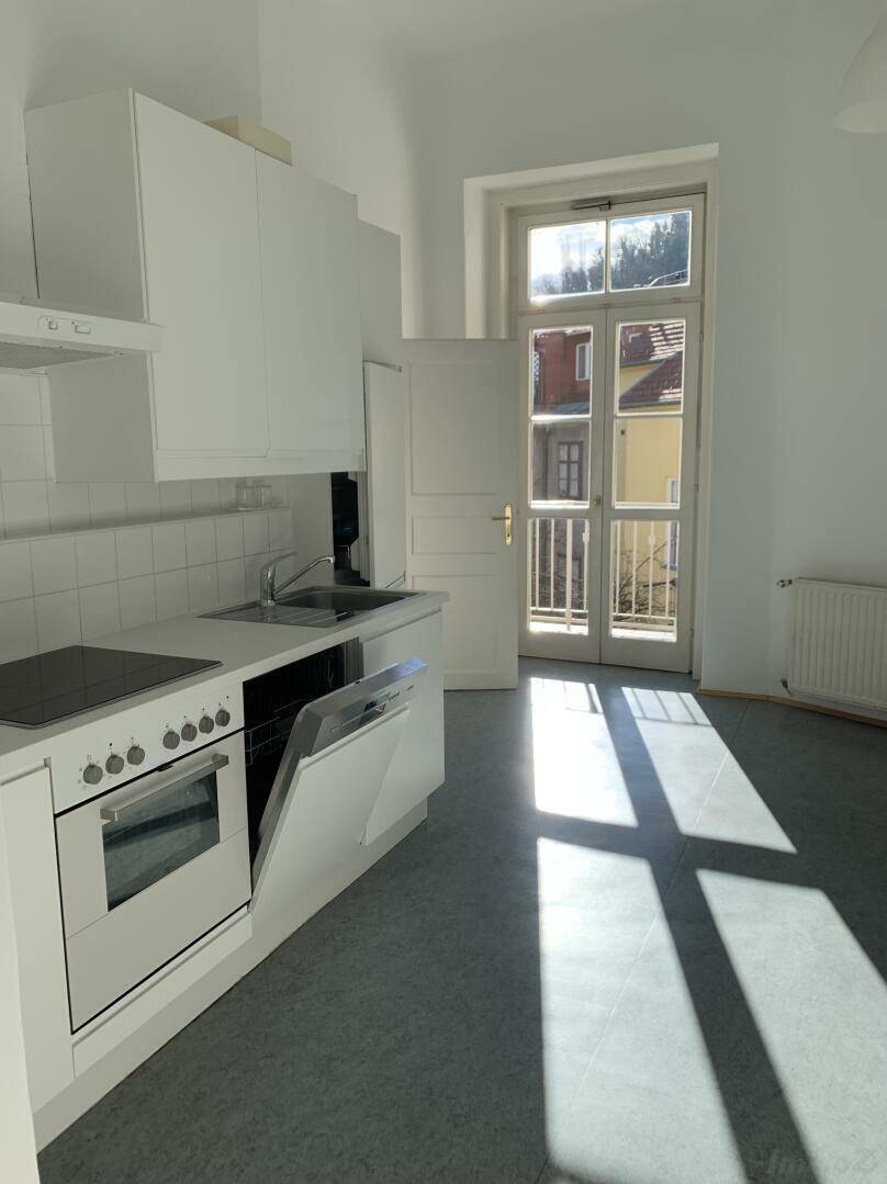 Helle Küche mit weißer Einbauküche, Geschirrspüler und Zugang zu einem kleinen Balkon.