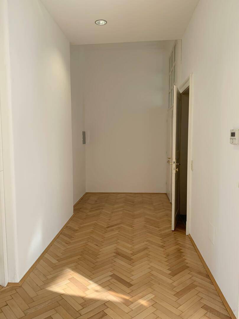 Heller Flur mit Fischgrätparkett und einer Tür, die zu einem weiteren Raum führt.