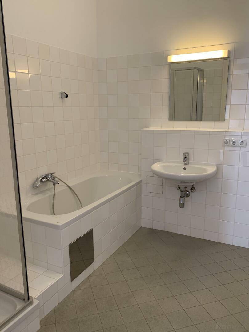 Gefliestes Badezimmer mit Badewanne, Waschbecken, Spiegel und Duschabtrennung.