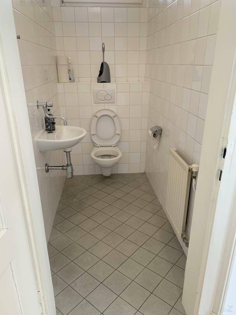 Kleines, gefliestes Gäste-WC mit Toilette, Handwaschbecken und Heizkörper.