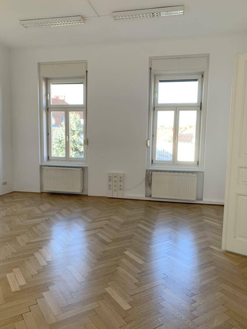 Geräumiges Zimmer mit zwei hohen Fenstern, Fischgrätparkett und viel Tageslicht.