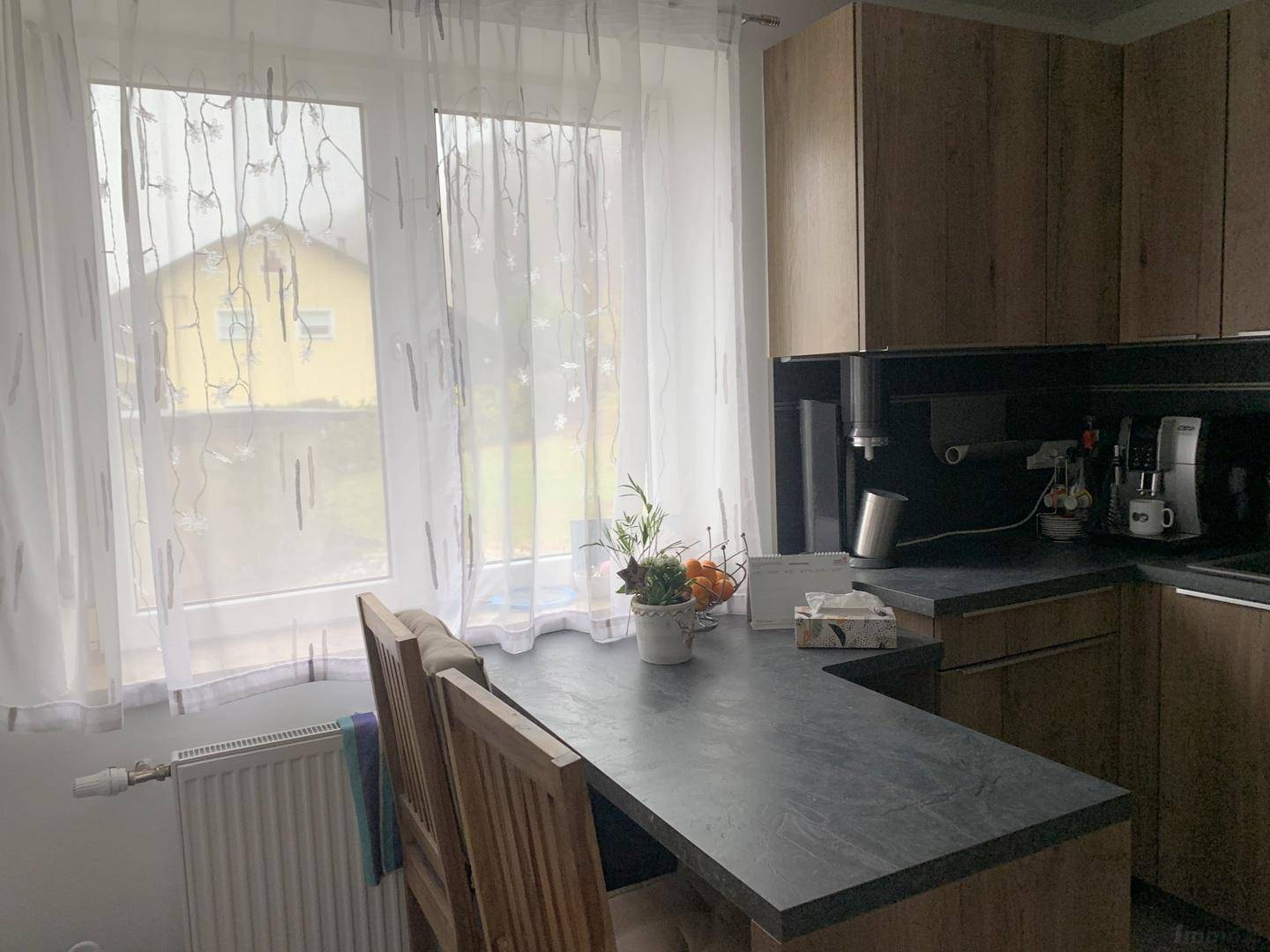 Küche mit Holzschränken, dunkler Arbeitsplatte und Blick ins Grüne durch das Fenster.