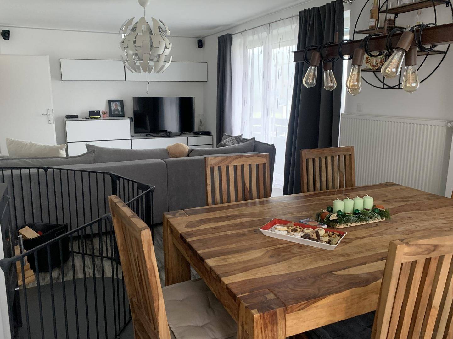 Geräumiger Wohn-Essbereich mit großem Holztisch, bequemer Couch und modernem Deckenlicht.