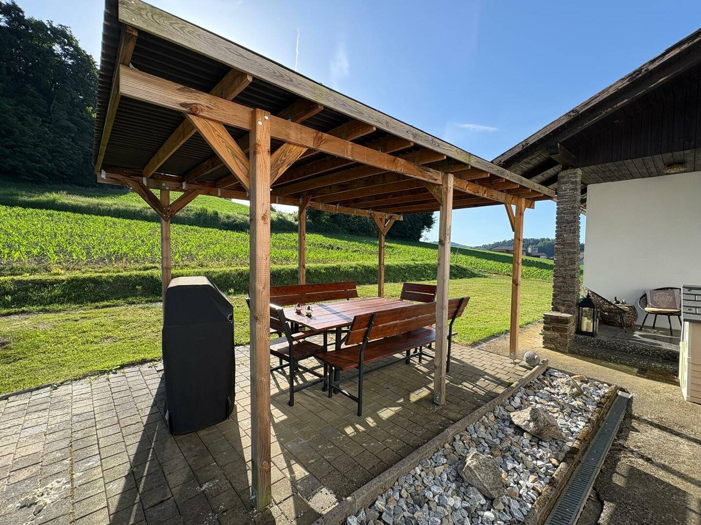 Gemütliche Holzpergola mit Esstisch und Bänken, ideal für Mahlzeiten im Freien mit Blick ins Grüne.