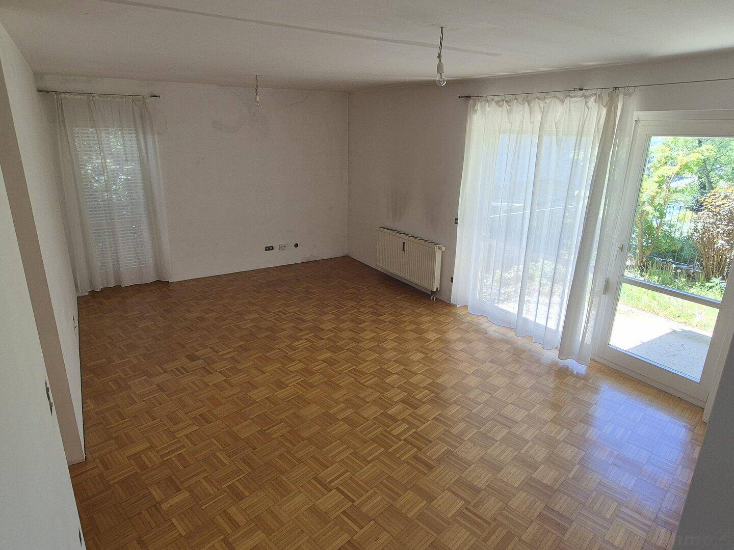 Geräumiges Wohnzimmer mit Parkettboden und großen Fenstern, die Zugang zum Außenbereich bieten.