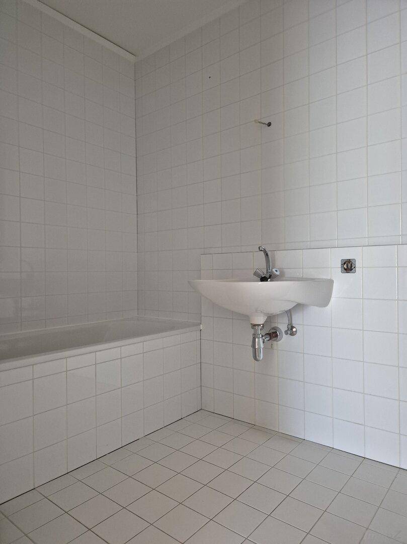 Badezimmer mit weißen Fliesen an Wänden und Boden, ausgestattet mit Waschbecken und Badewanne.