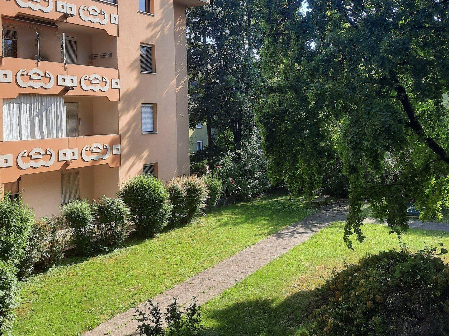 Außenansicht eines Mehrfamilienhauses mit gepflegter Grünfläche und Bäumen.