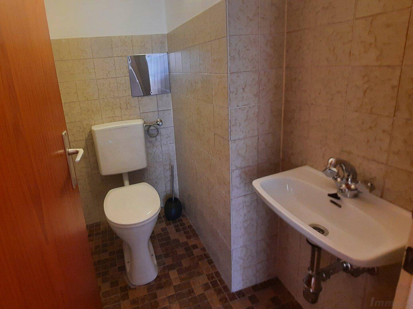 Separate Toilette mit Waschbecken und Fliesen an Wänden und Boden.