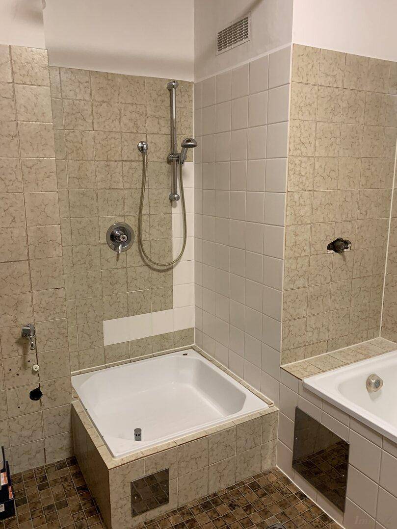 Badezimmer mit Duschwanne und Fliesen an Wänden und Boden in hellem Farbton.