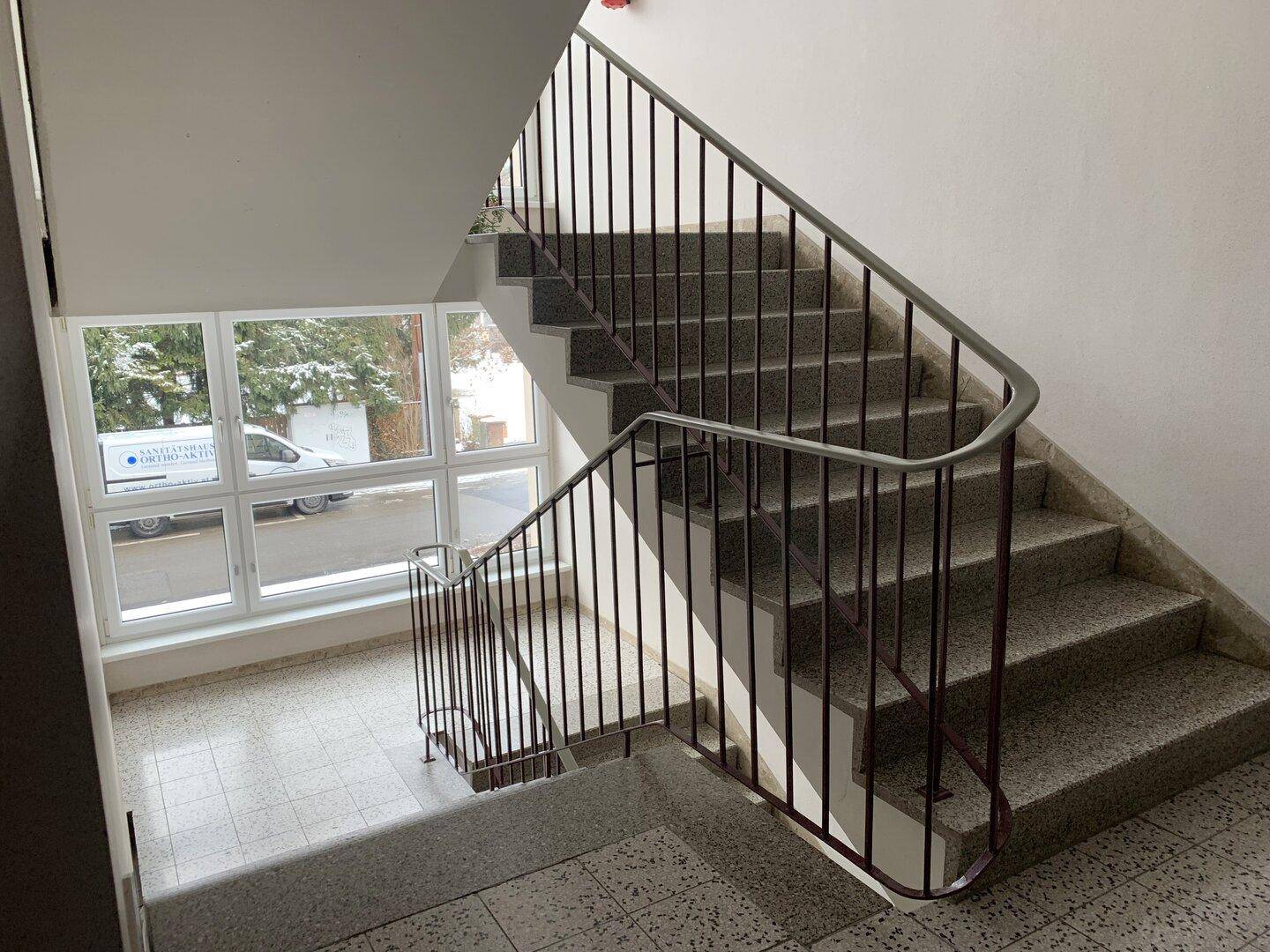 Helles Treppenhaus mit Terrazzoboden und Geländer, das zu den oberen Etagen führt.