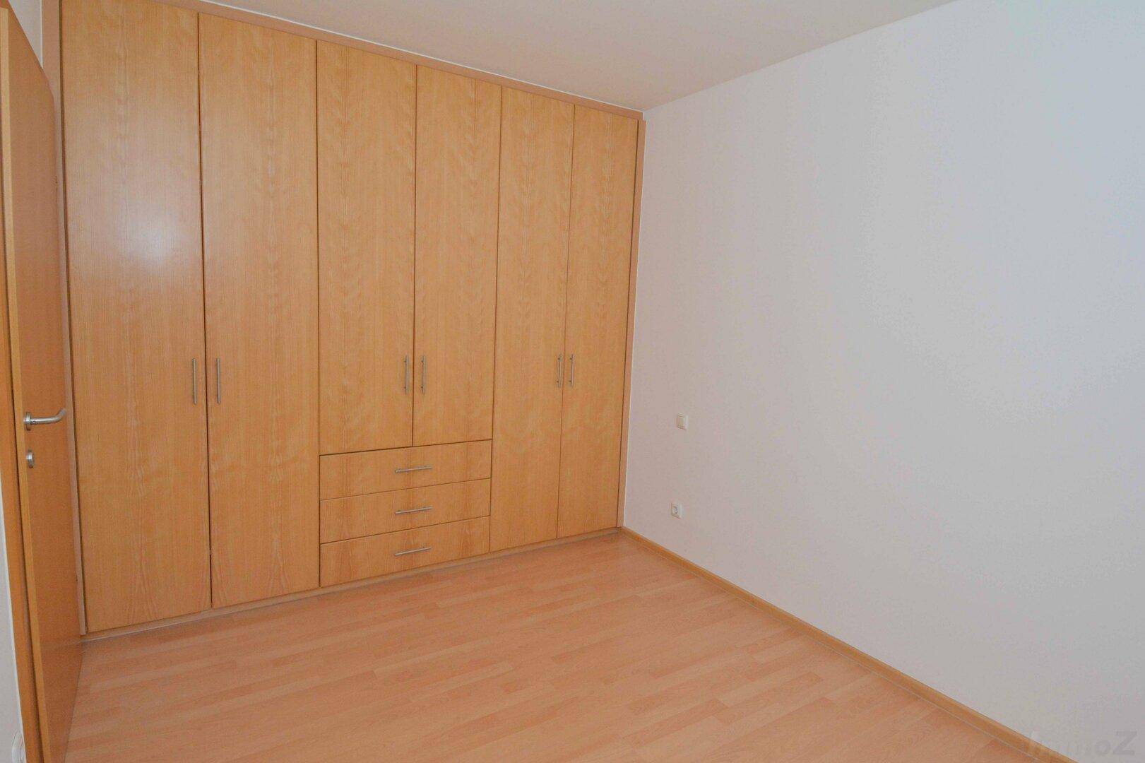 Schlafzimmer mit großem Einbauschrank aus hellem Holz und Laminatboden.