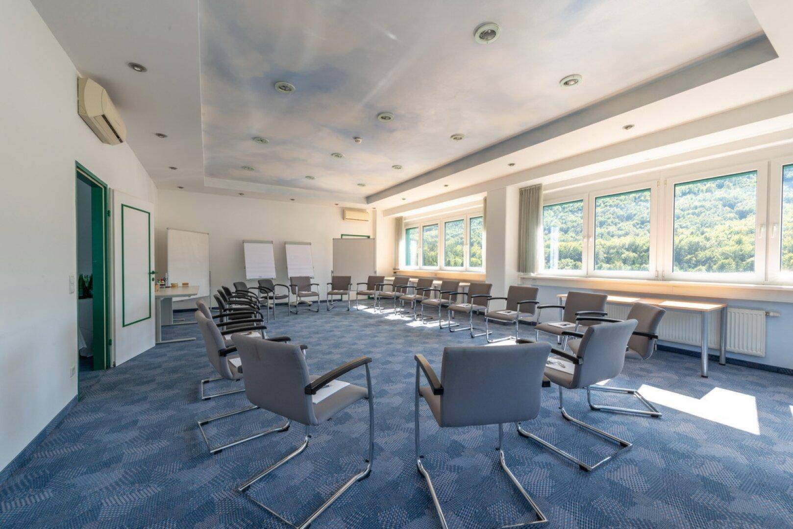 Großer Konferenzraum mit blauer Teppichboden und weitem Blick auf die grüne Berglandschaft.