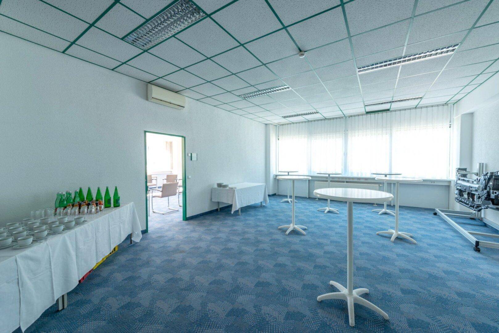 Vielseitiger Veranstaltungsraum mit Stehtischen, Getränkebuffet und blauer Teppichboden.