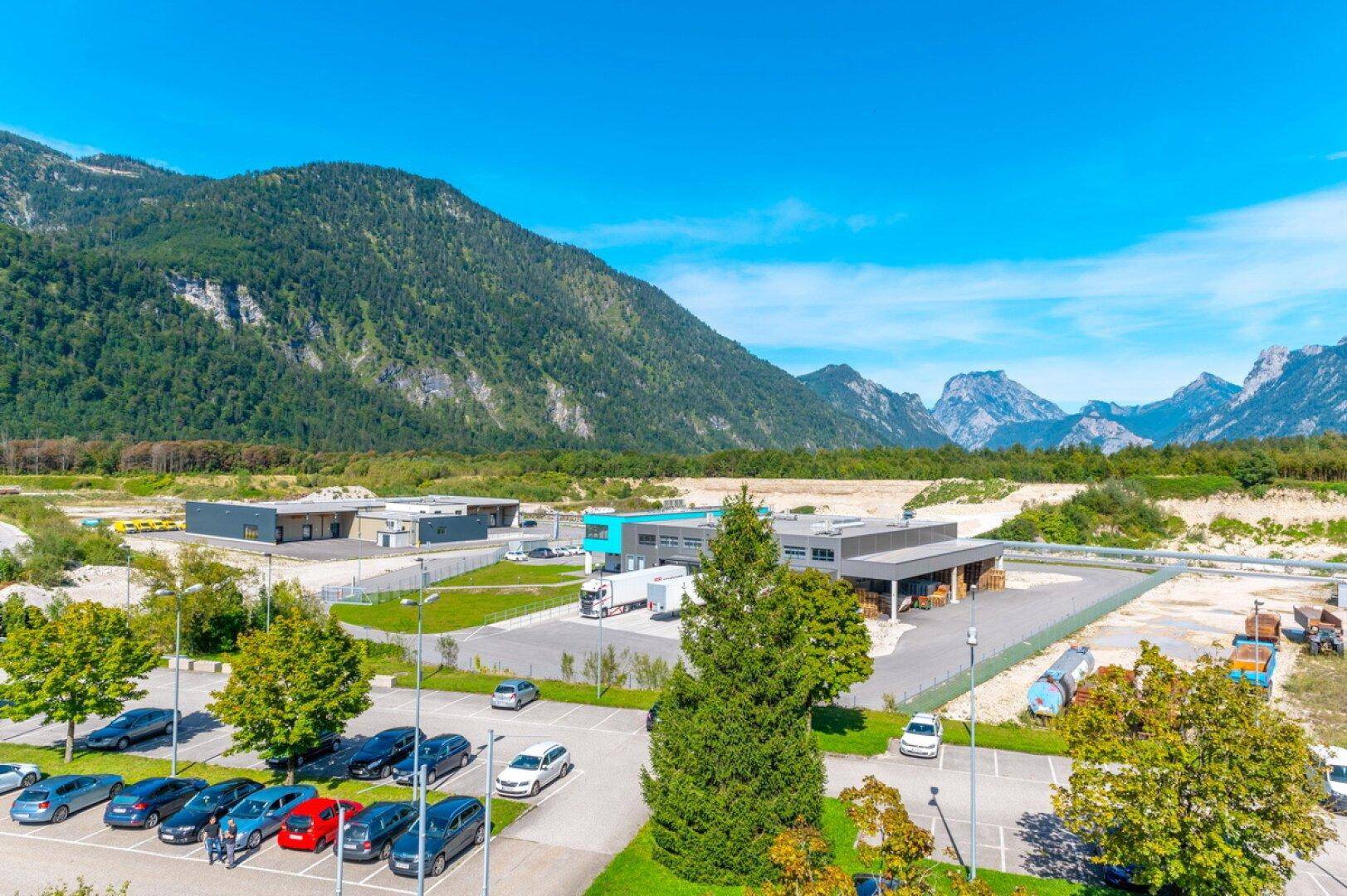 Übersicht einer Gewerbefläche mit mehreren Gebäuden, Parkplätzen und umliegenden Bergen.