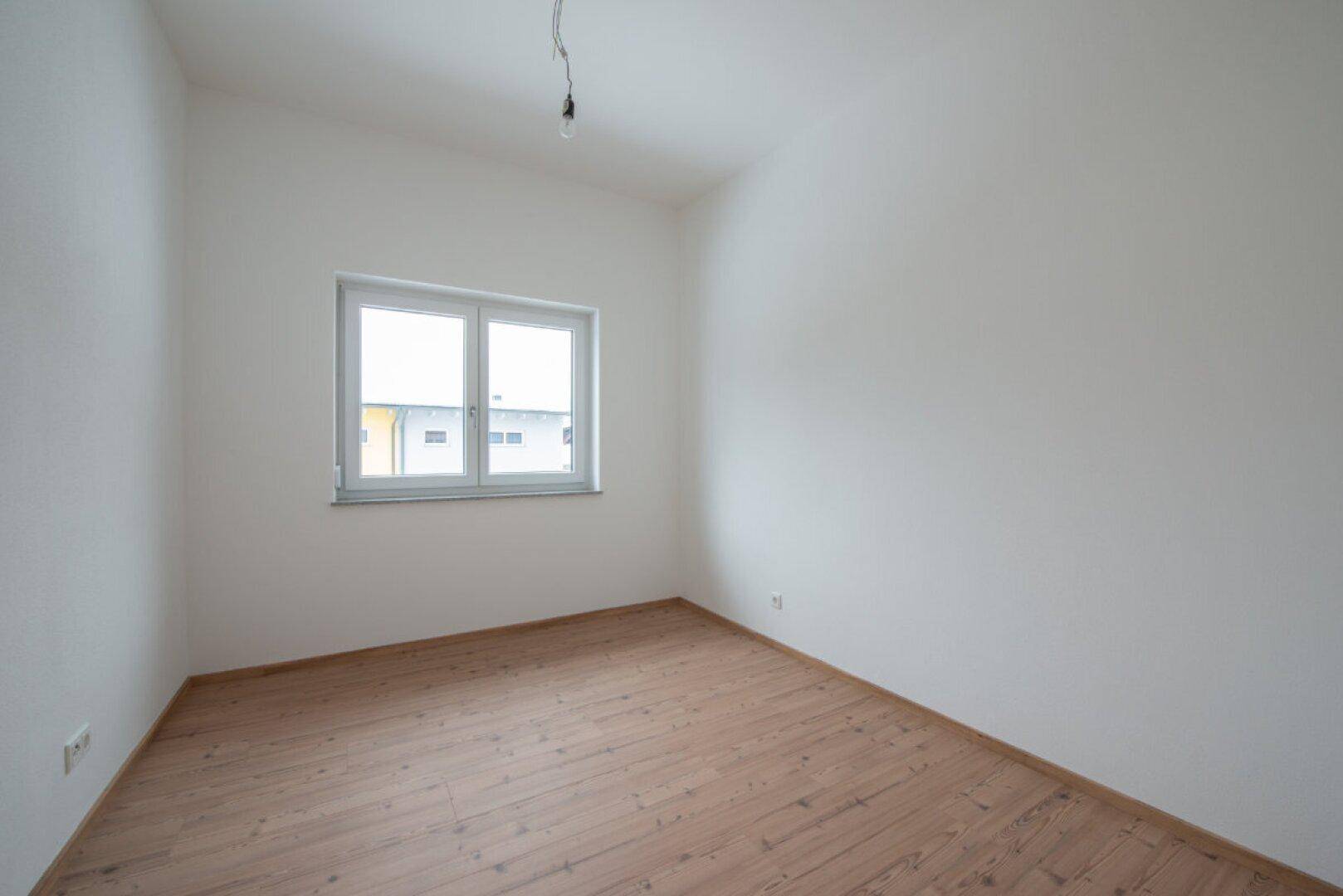 Leeres Schlafzimmer mit Holzboden und einem großen Fenster für viel Tageslicht.