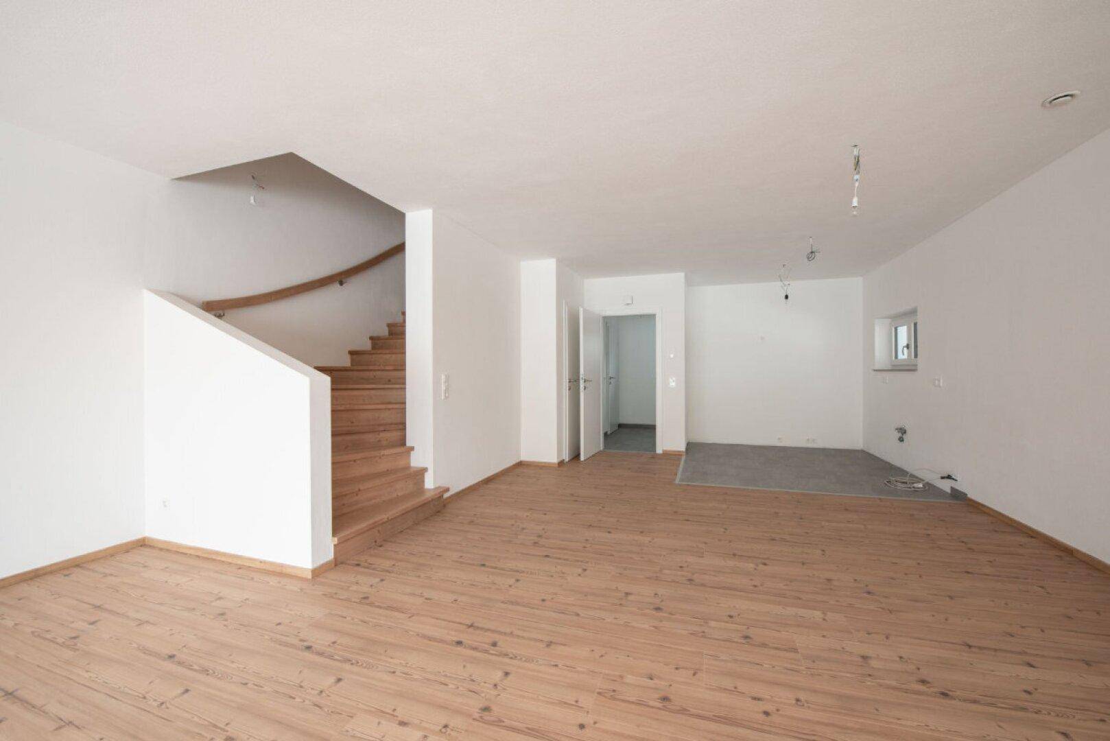 Geräumiger Wohnbereich mit Holztreppe, Holzboden und vorbereitetem Küchenbereich.