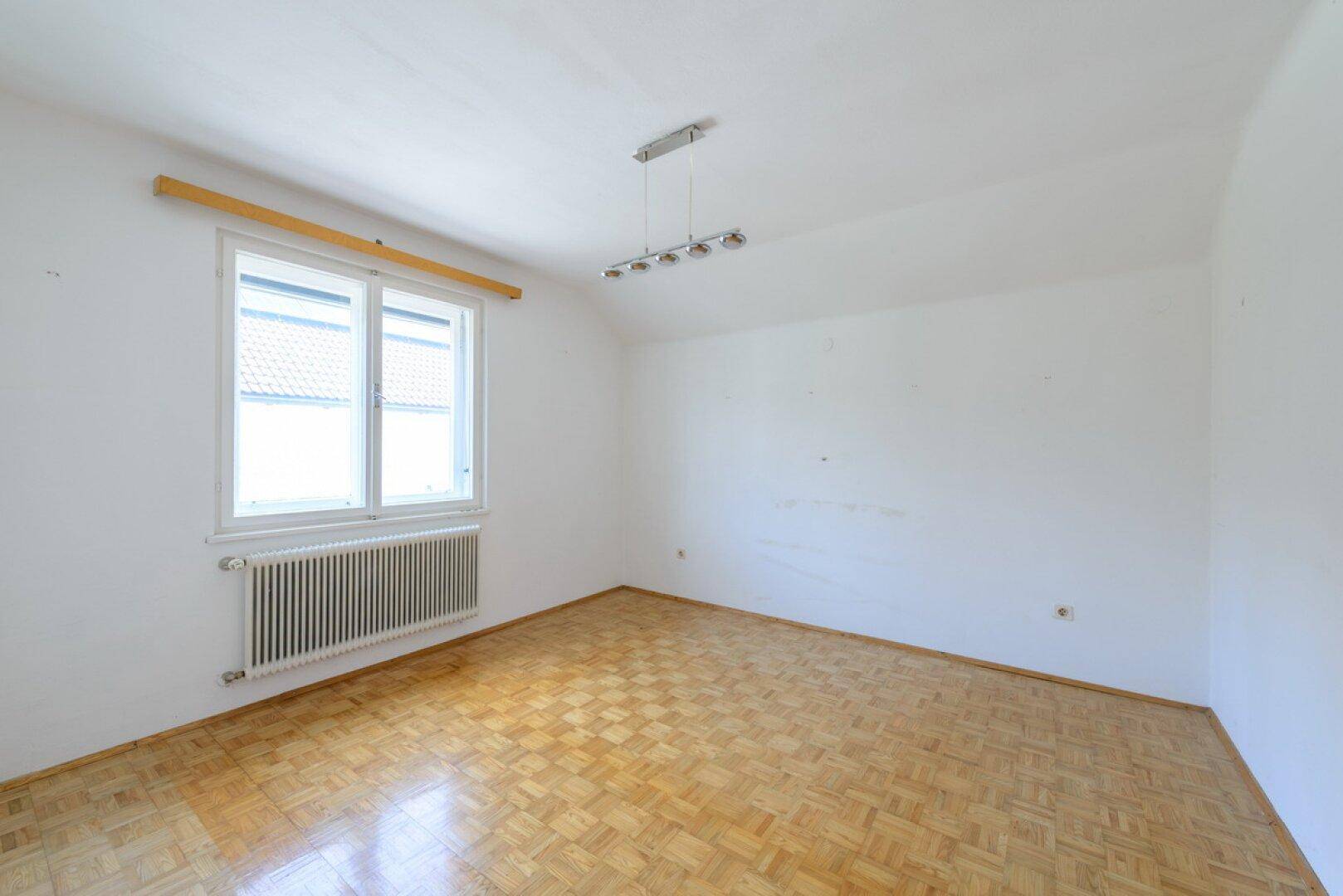 Helles Schlafzimmer mit Parkettboden und Fenster, bietet viel Tageslicht.