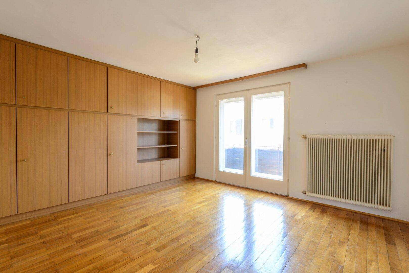 Geräumiges Schlafzimmer mit Einbauschränken, Parkettboden und Zugang zum Balkon.