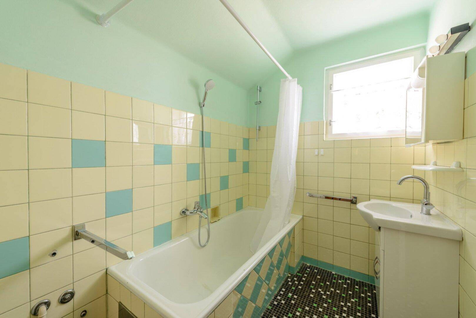 Badezimmer im 80er-Jahre-Stil mit Badewanne, Waschbecken und farbigen Fliesen.
