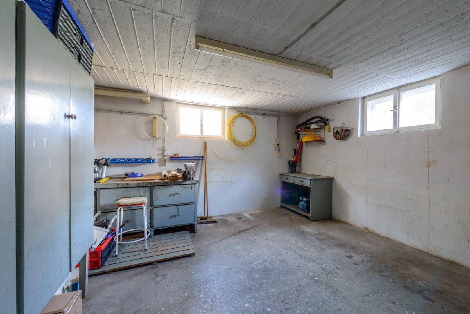 Geräumiger Hobbyraum im Keller mit Werkbank, Stauraum und Fenstern für Tageslicht.