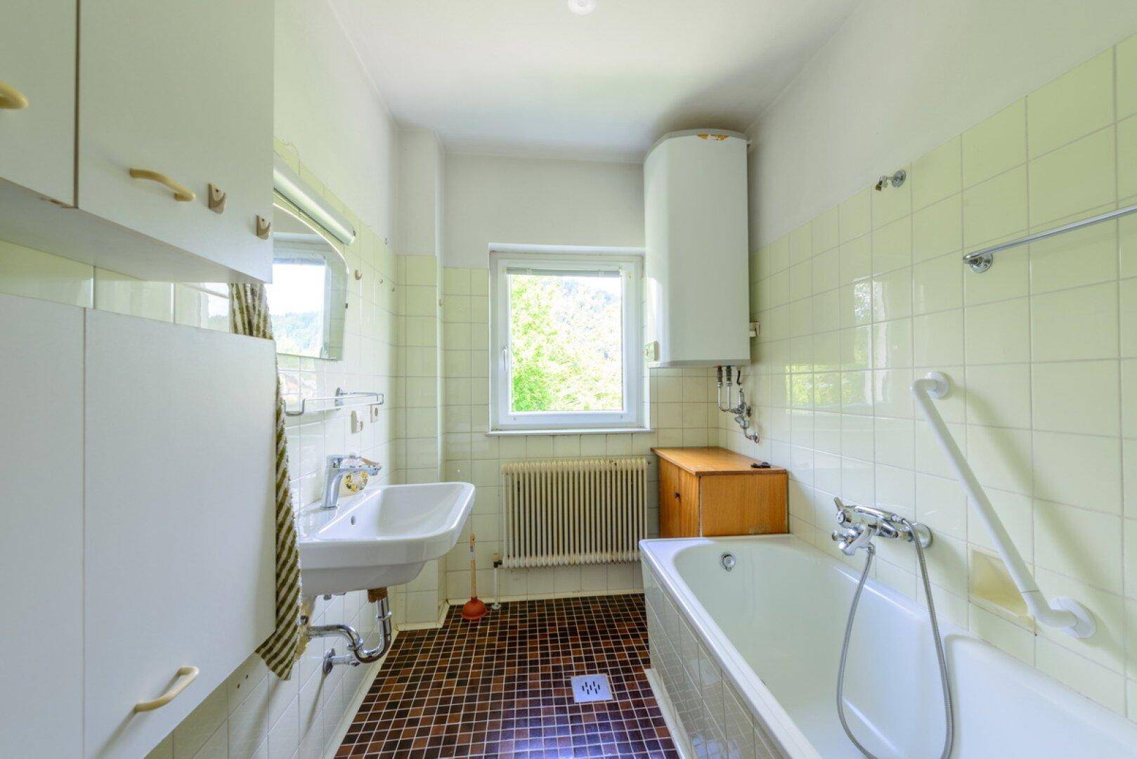 Badezimmer im 80er-Jahre-Stil mit Badewanne, Waschbecken und Fenster.